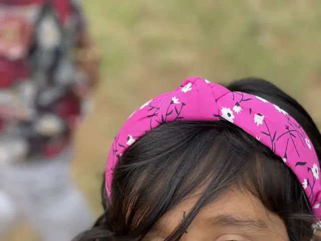 A girl in a bright pink headband looks up into the camera with a wide open-mouthed laugh