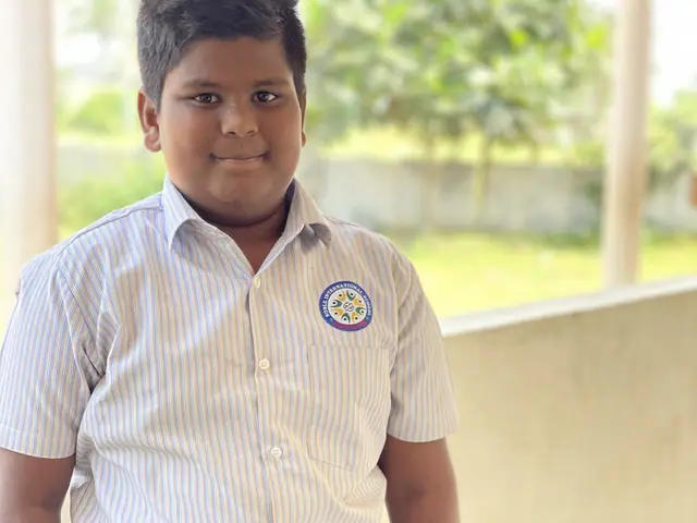 A boy in the school's white shirt stands in an open corridor of the school building, hands folded