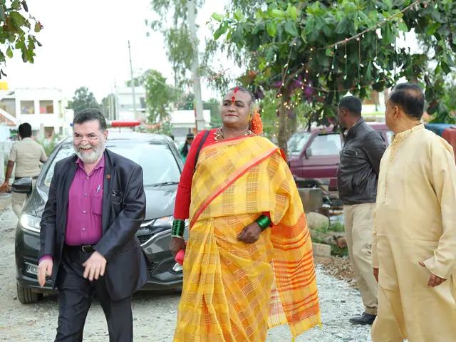 A visitor in a dark suit stands smiling beside a host draped in a yellow silk shawl