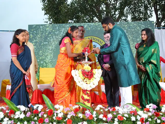 Guests and a small girl gather at the garlanded brass lamp on the decorated stage