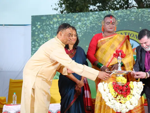 Two men lean in together to light the tall garlanded brass lamp at the centre of the stage