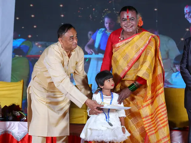 A very small girl reaches up to accept her prize from a man in an orange-bordered silk shawl