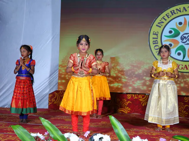 Two girls in classical dance costume with gold jewellery hold a pose beneath the school crest