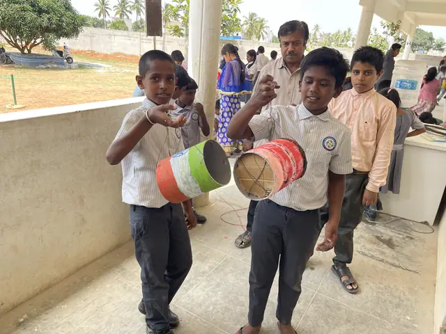 Two boys on an open corridor holding brightly painted hand-made drums, the nearer one grinning at the lens