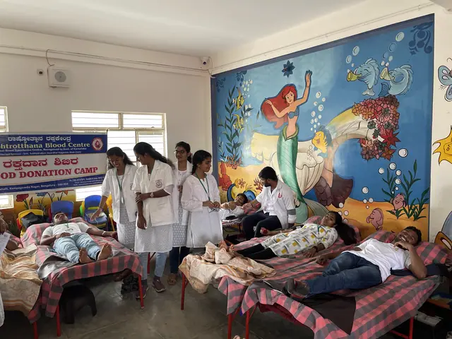Blood donation camp in a hall: donors on beds attended by volunteers in white coats