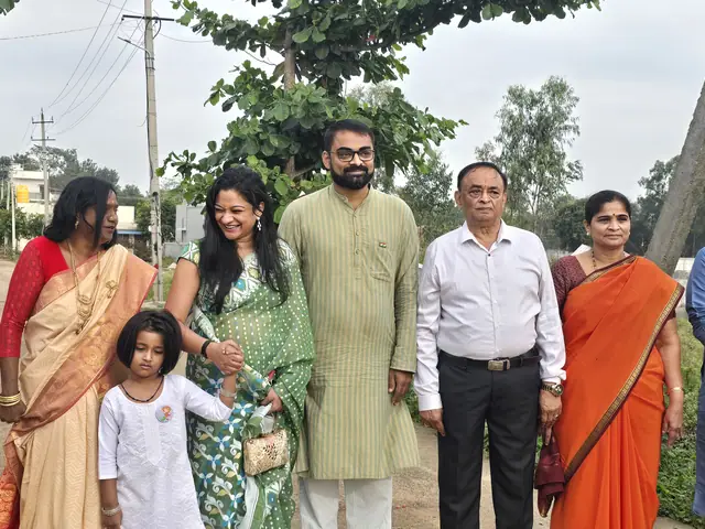 Eight adults in kurtas and saris with two children posed on a village road, green trees behind