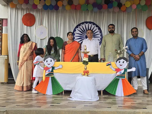 Adults in formal dress behind a table draped in tricolour cloth, Ashoka chakra roundel behind