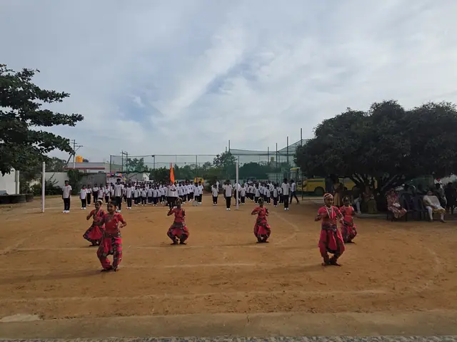 Marching students in white and dancers in red costumes under a large spreading tree