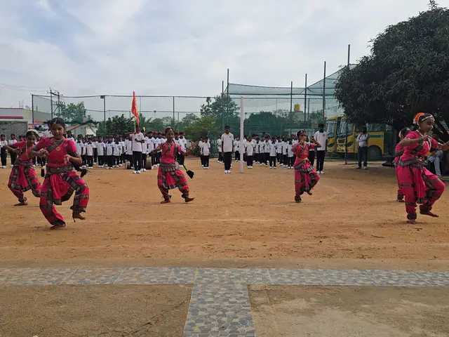 Girls in red folk costumes dance mid-step while rows of uniformed students watch