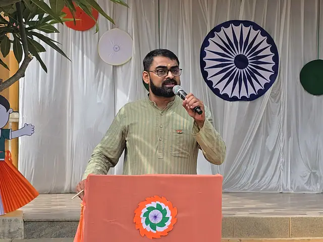 A speaker framed beside a large Ashoka chakra roundel on white drapes