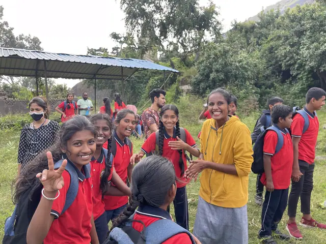 Five girls laughing and flashing peace signs on a grassy hillside, faces lit and clear