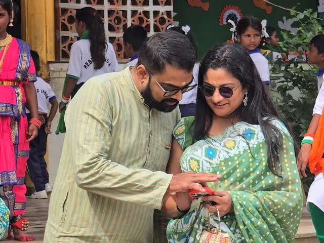 A man in a pale kurta and a woman in a green sari among girls in bright pink folk costumes