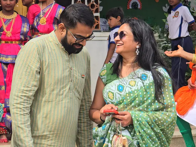 A woman in a green sari gestures and laughs beside a man in a kurta, costumed girls around them