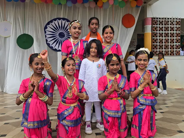 Pink-costumed girls posed together with folded hands, uniformed students behind