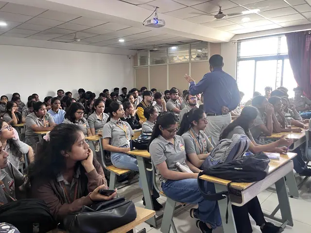A packed college classroom from the back, dozens of students facing a speaker