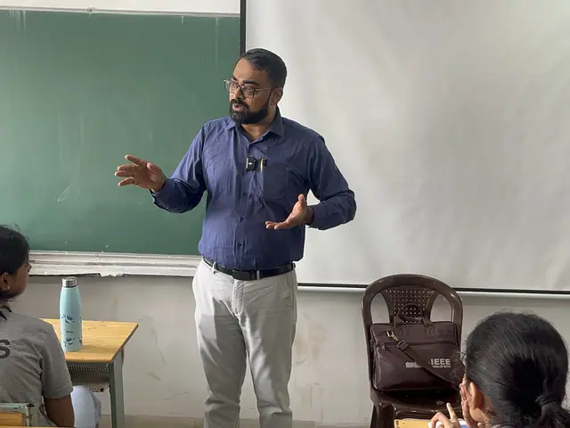 The lecturer gesturing in front of the green board, students' heads at the bottom edge