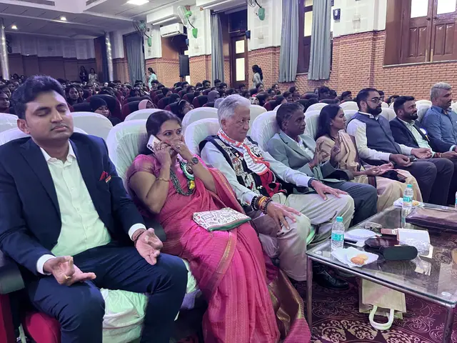 Front row of an auditorium with garlanded guests seated, packed rows behind
