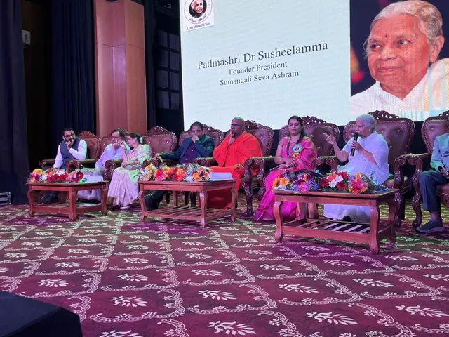 The auditorium dais with guests behind a low table of flowers, deep red curtains at the sides