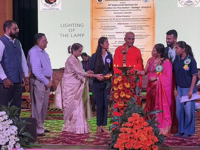 Lamp lighting on stage: a woman in a sari leans in to light the tall brass lamp