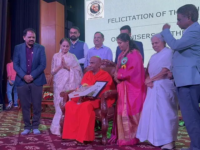 An elderly woman seated in a red-draped chair is honoured by guests standing around her