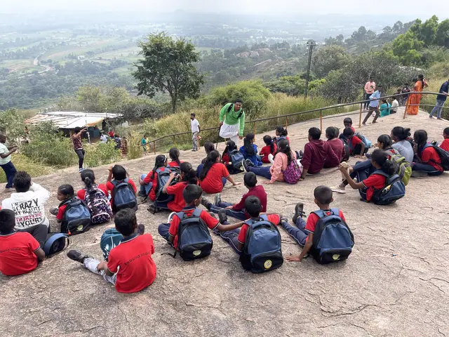 Fifty students sitting in a loose ring on a bare rock summit with a green valley behind