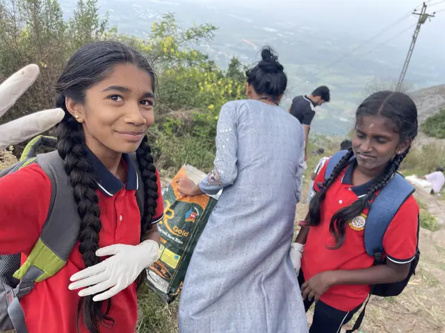 A girl in plaits smiles sidelong at the camera holding a litter bag and wearing white work gloves