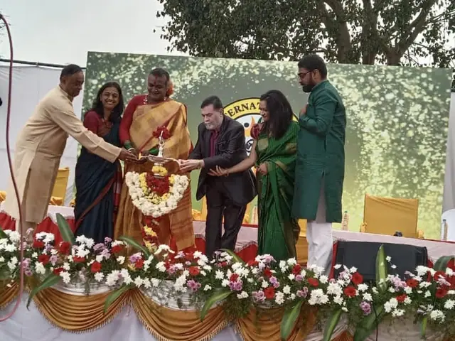 Six adults light a ceremonial lamp together on a flower-decorated stage