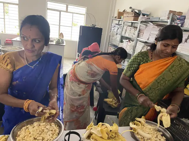 Three women in vivid saris working shoulder to shoulder over trays at a long counter