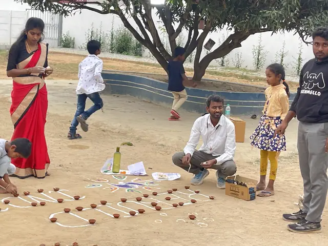 A man crouches to lay out rows of small clay lamps under a spreading tree, children helping