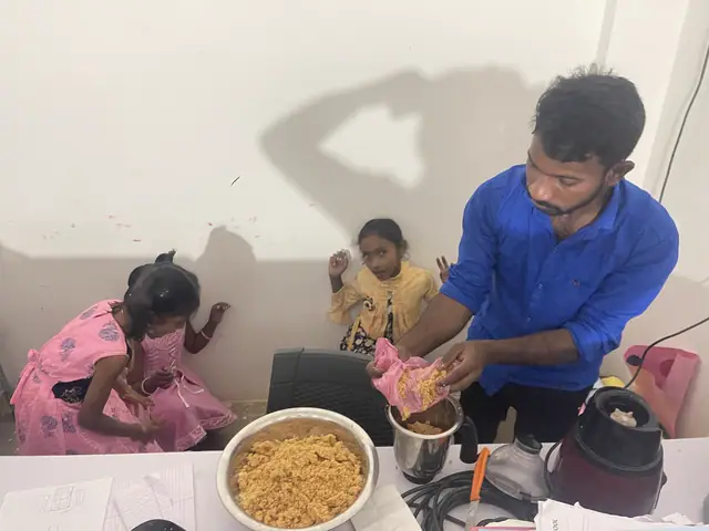 Two small girls reach up to help a man at a table of prepared food