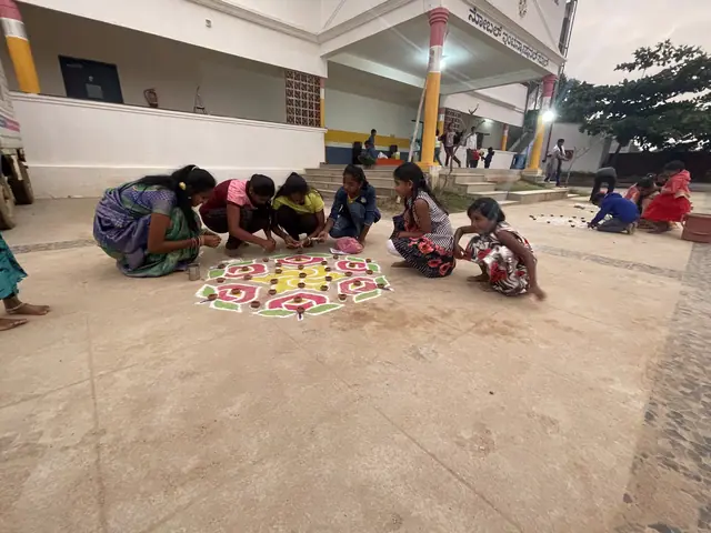 Girls and women bent over two large coloured rangoli designs on the school forecourt