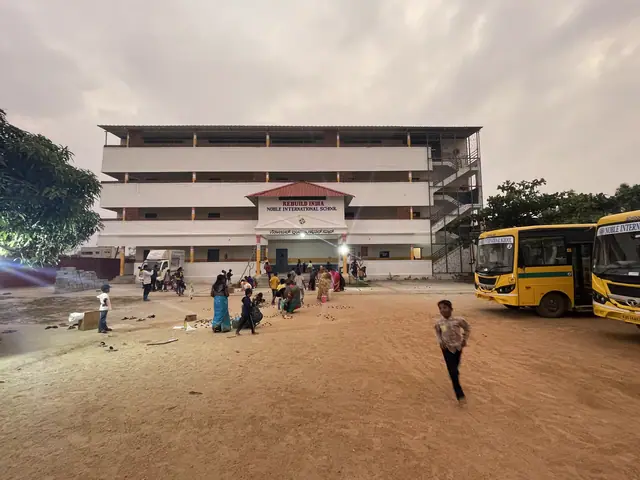 Wide dusk view of the school block with its red name board, two yellow buses and a pink evening sky