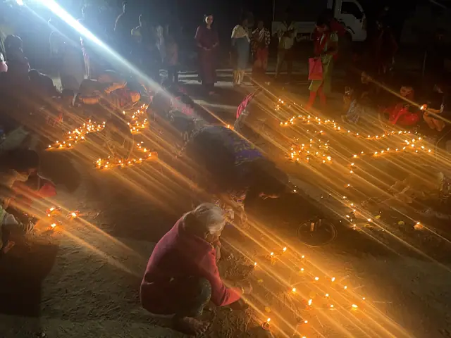 Long converging rows of burning diyas fill the frame, a woman at the far end still lighting them