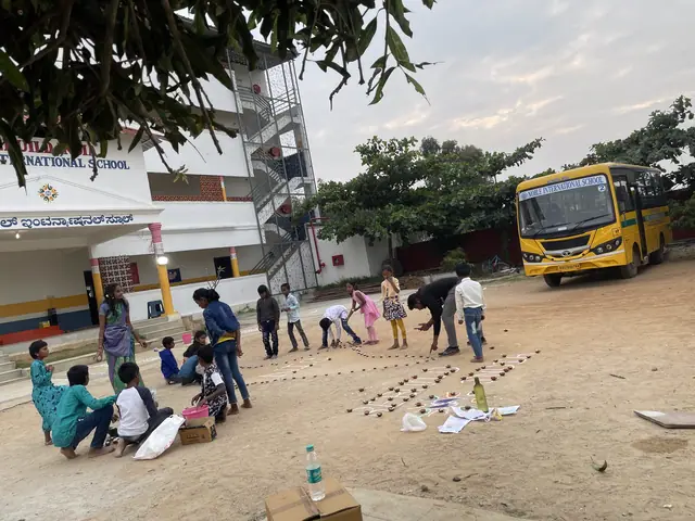 Wide view of the school compound at dusk, a yellow bus beside the building, children laying out lamps