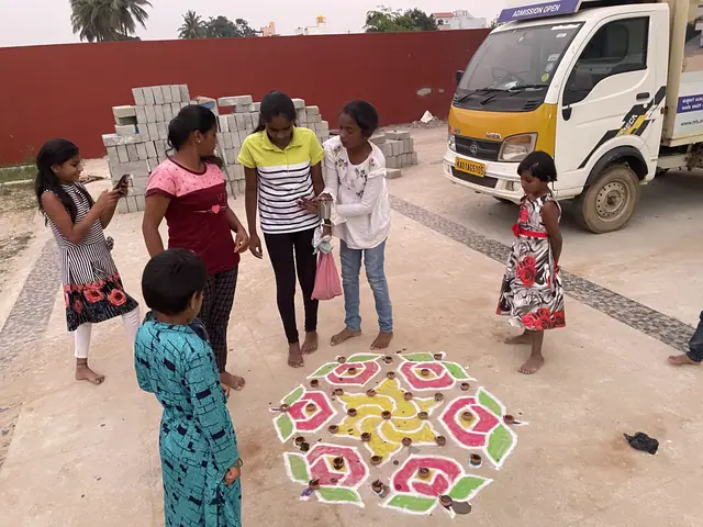 Six girls and a boy in a loose circle looking down at a freshly finished pink and green rangoli