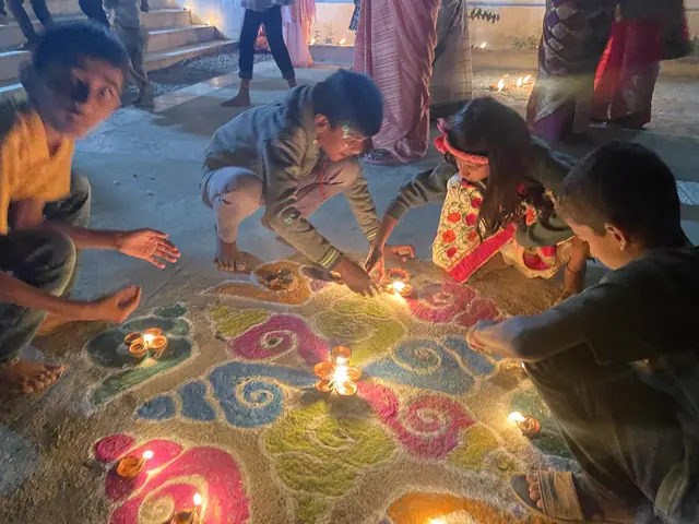 Children kneeling to light the last of hundreds of oil lamps arranged around a large coloured rangoli