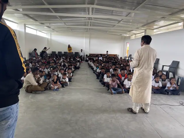 Wide interior of the school hall with several hundred children seated on the floor in rows