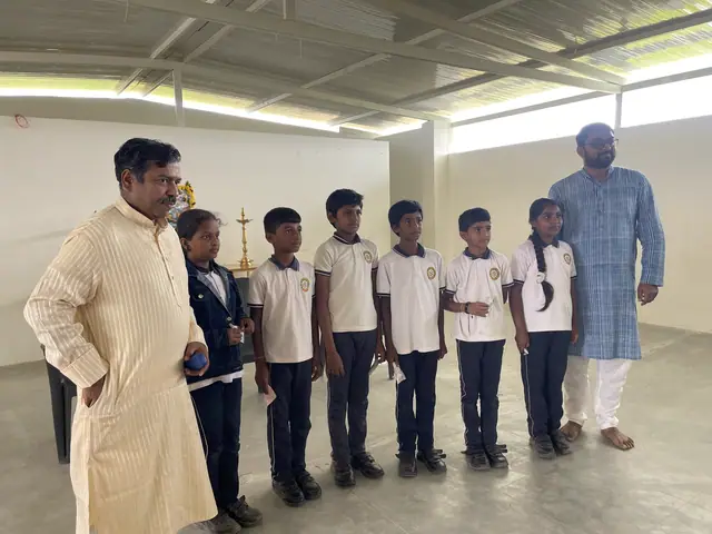 Five boys lined up in the hall between two men in kurtas beside a lit brass lamp