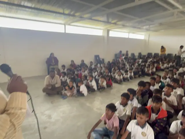 Very wide view of the hall packed with hundreds of children seated on the floor