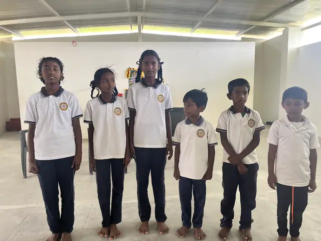 Six children in white uniform standing barefoot in a line facing the camera