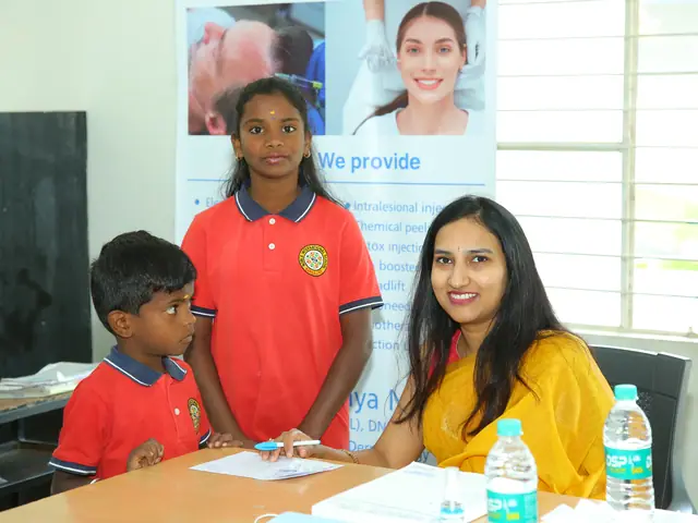 A boy and an older girl at a doctor's desk in a classroom, the young doctor smiling up at them