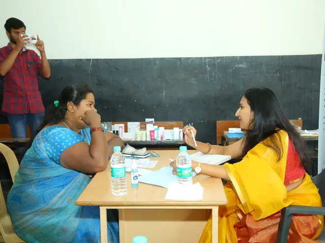 A woman in a blue sari in consultation with a doctor in a classroom, medicine boxes between them