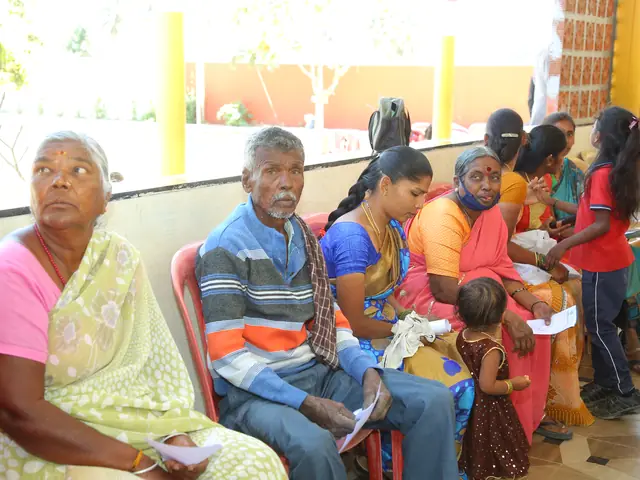 An elderly couple seated waiting in a classroom while a young child stands beside them