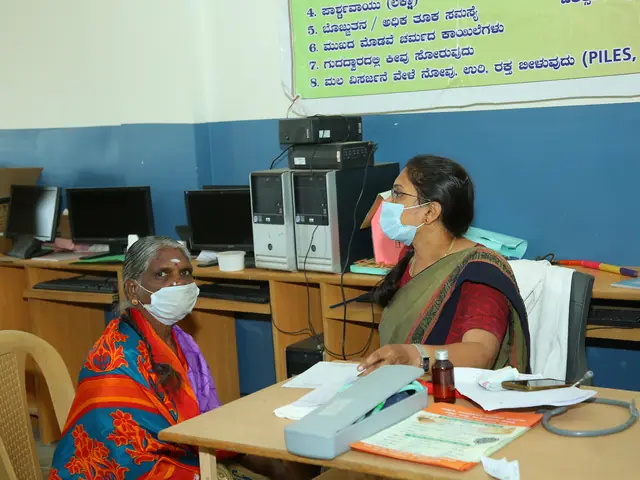 An elderly woman seated opposite a health worker with files and equipment between them