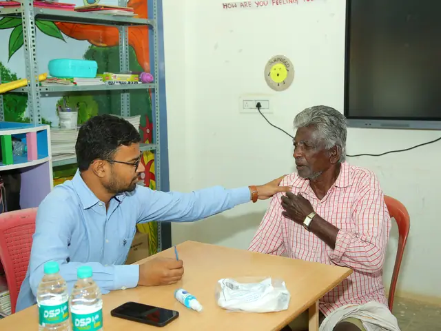 A doctor leans across a small table to examine an elderly man in a brightly painted room