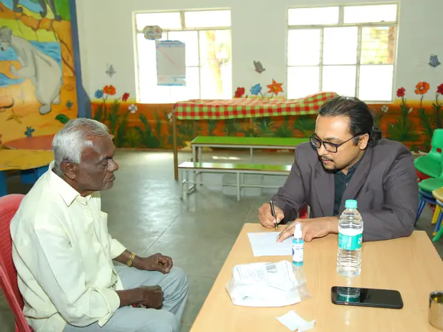 An elderly man sits calmly opposite a man writing at a table in a bright whitewashed room