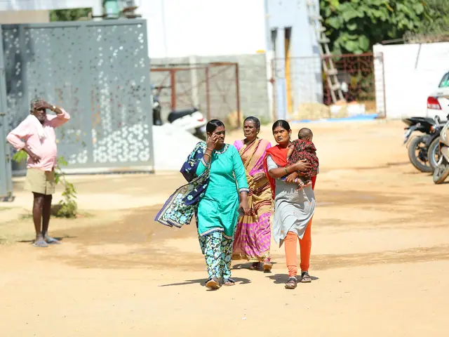 A woman in a green sari walks a dirt road toward the camera with a child at her side