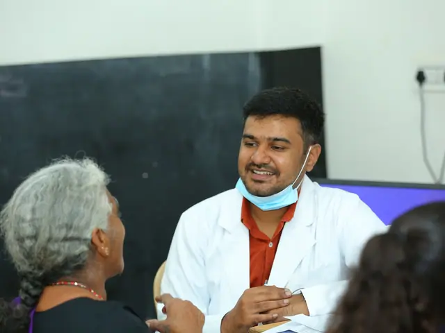 A young doctor in a white coat smiles while listening to a grey-haired woman across a desk