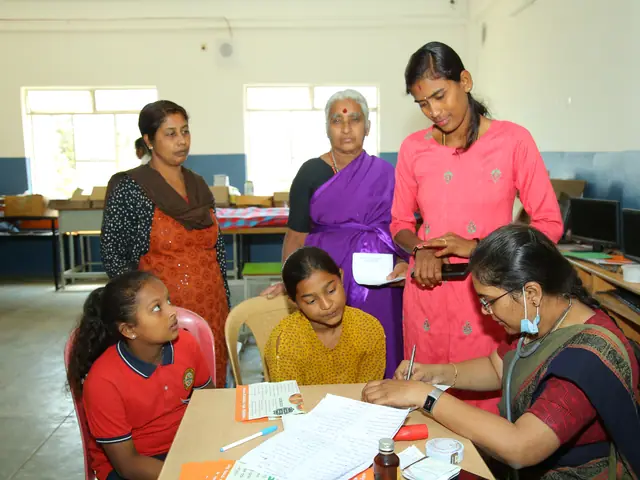 Village women and schoolgirls work at tables in the computer room, monitors along the far wall