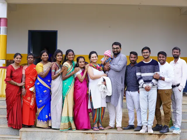 Row of staff in bright saris and shirts posed along the veranda of the school building